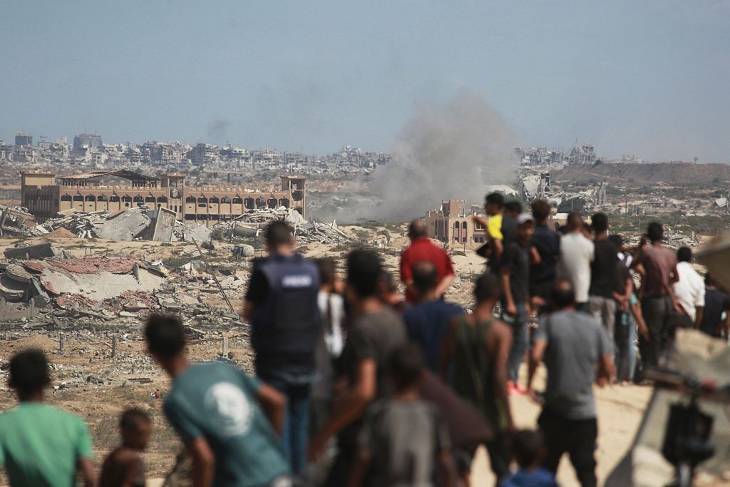 Palestinians watch smoke billowing during Israeli strikes upon arrival on a coastal path northwest of Nuseirat refugee camp as they are displaced southward from Wadi Gaza on Wednesday. Israel